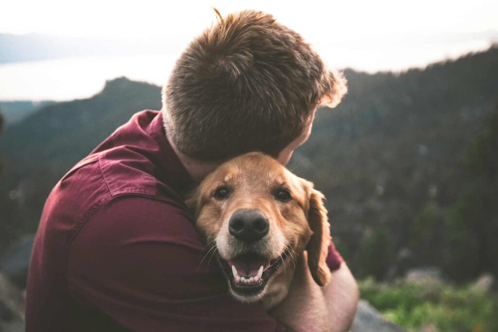 A man looking away from the camera, hugging his Diabetic dog.