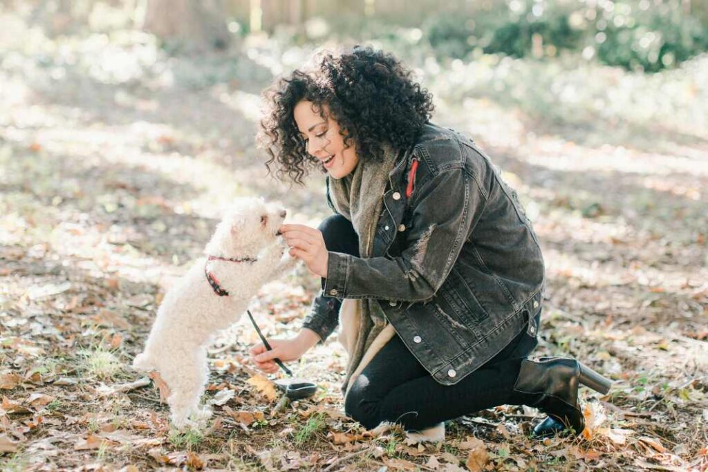 A woman giving her dog a treat in a wooded area.